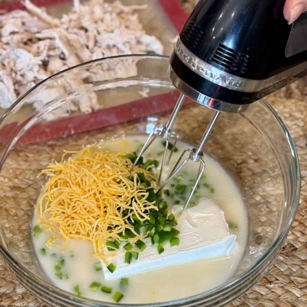 Whipping cream cheese, broth and cheese in a bowl.