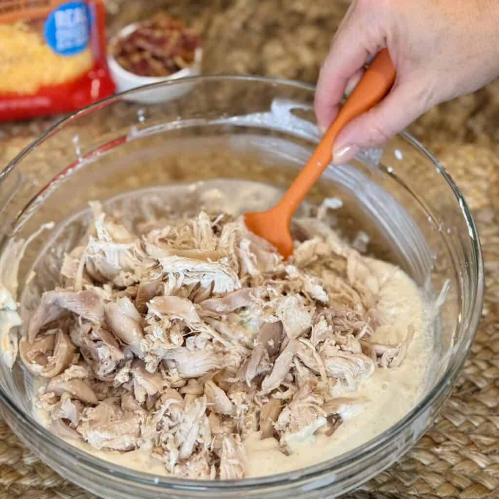 Adding chicken to a bowl with cream cheese and broth.