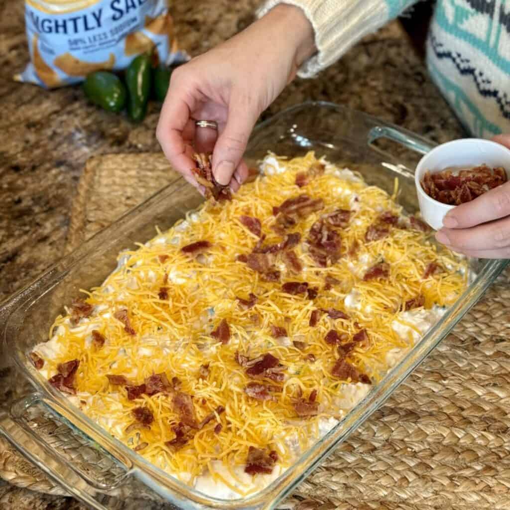 Sprinkling bacon and cheese on a casserole.