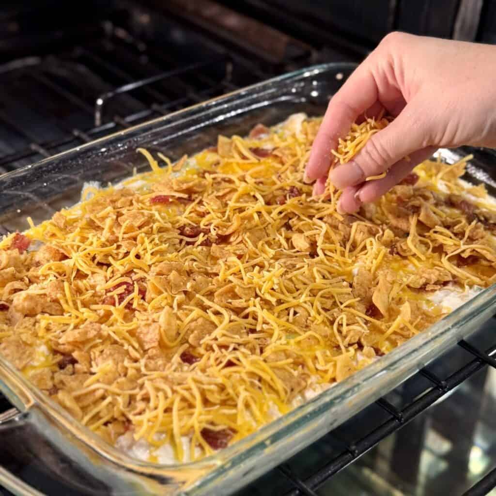 Sprinkling fritos, cheese and bacon on a casserole.