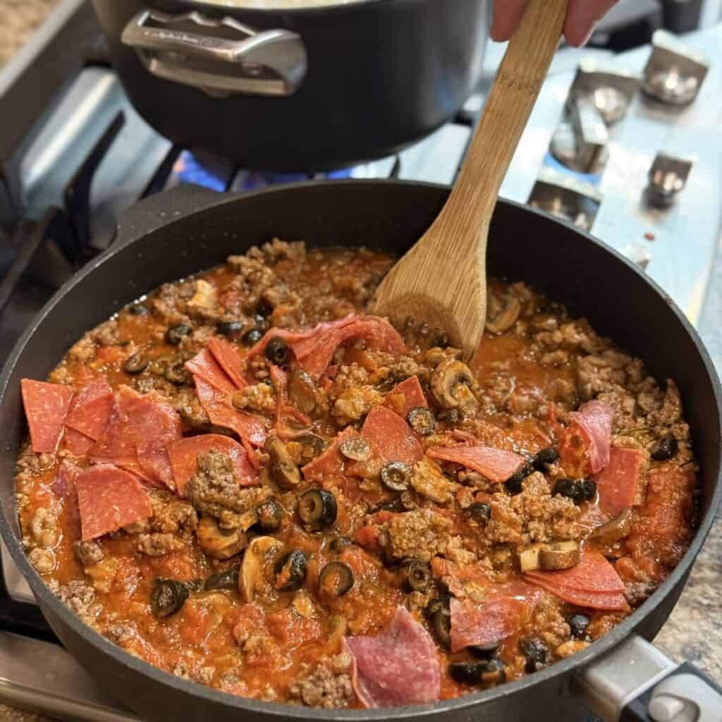 Mixing the sauce for pizza pasta in a pan.