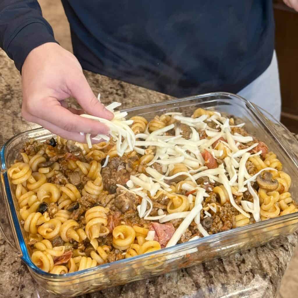 Adding cheese to the top of a pizza pasta recipe.