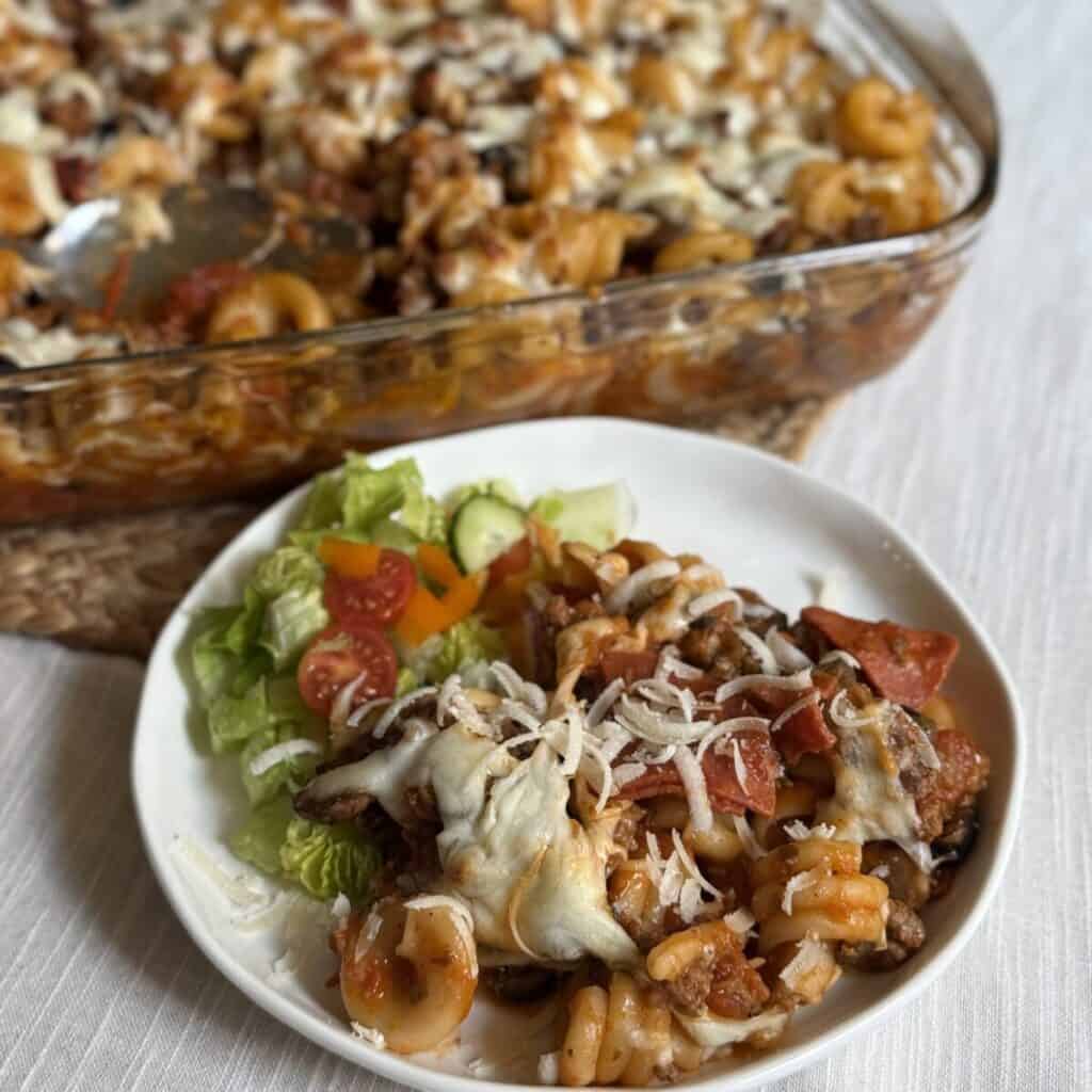 A serving of pizza pasta recipe on a plate with a salad.