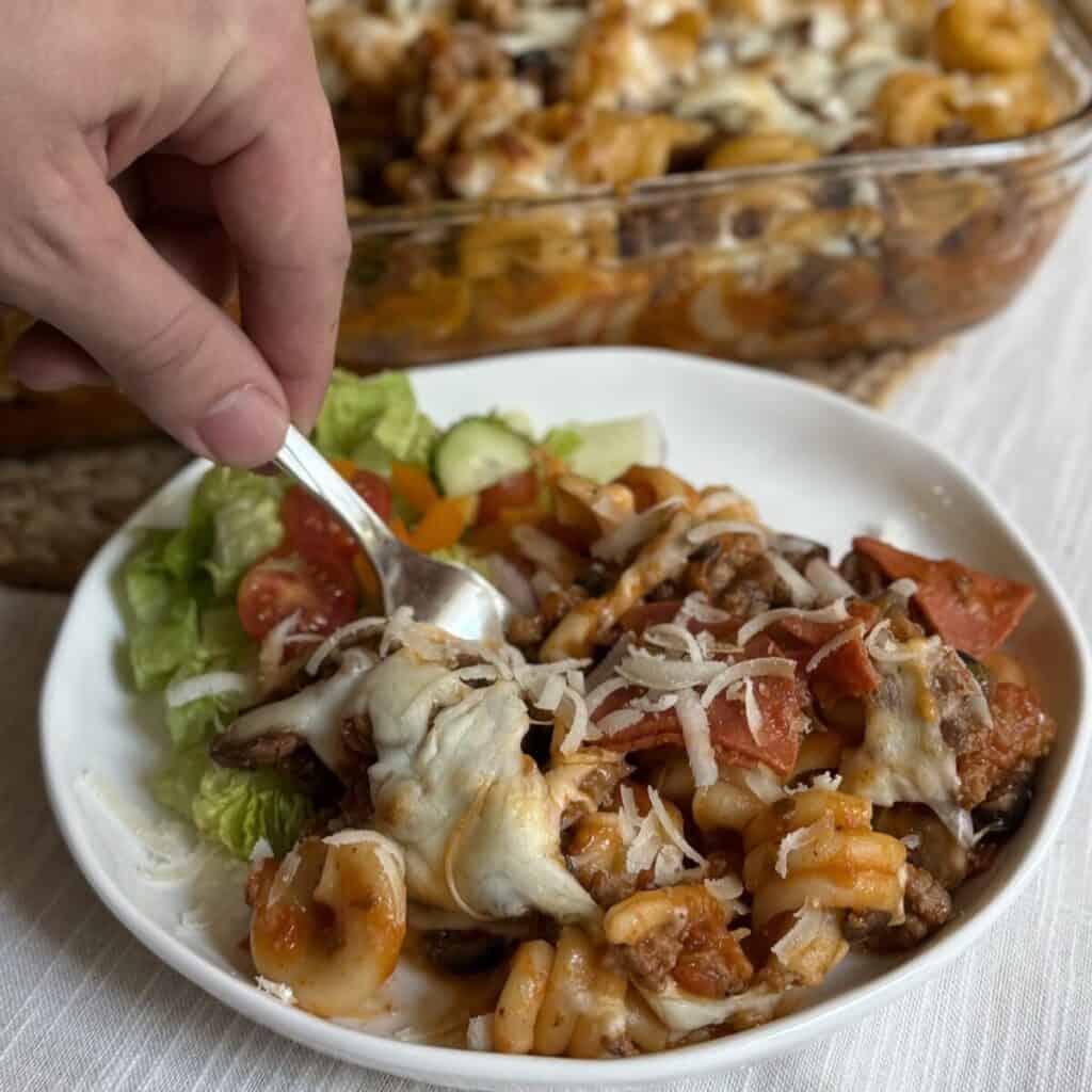 A serving of pizza pasta recipe on a plate with a salad.