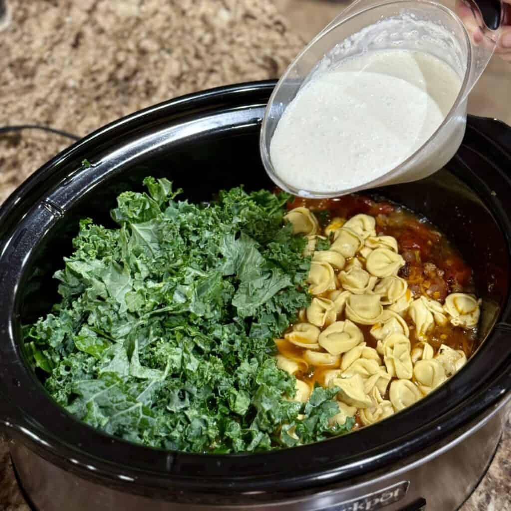 Stirring crockpot sausage tortellini soup in a crockpot.