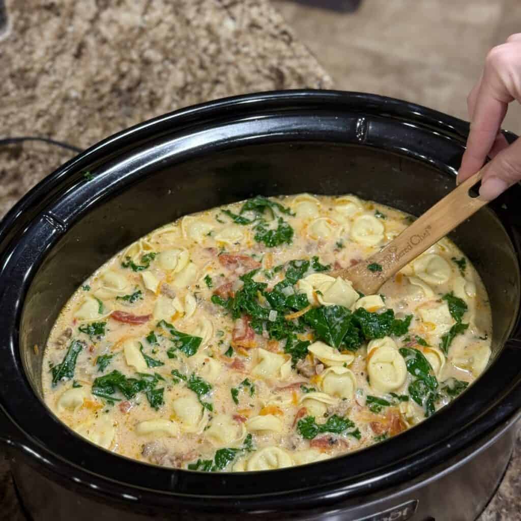 Stirring crockpot sausage tortellini soup in a crockpot.