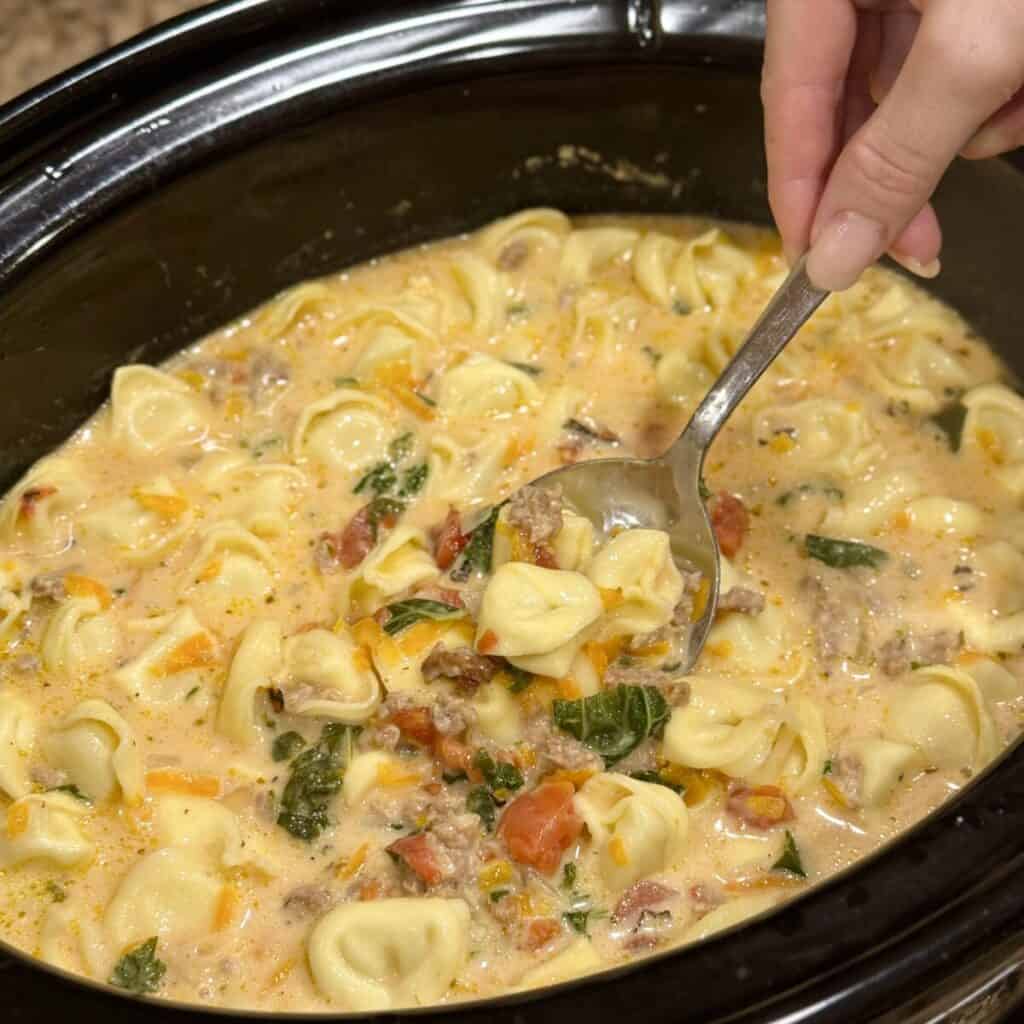 Stirring crockpot sausage tortellini soup in a crockpot.