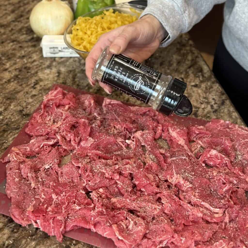 Seasoning shaved steak on a cutting board.