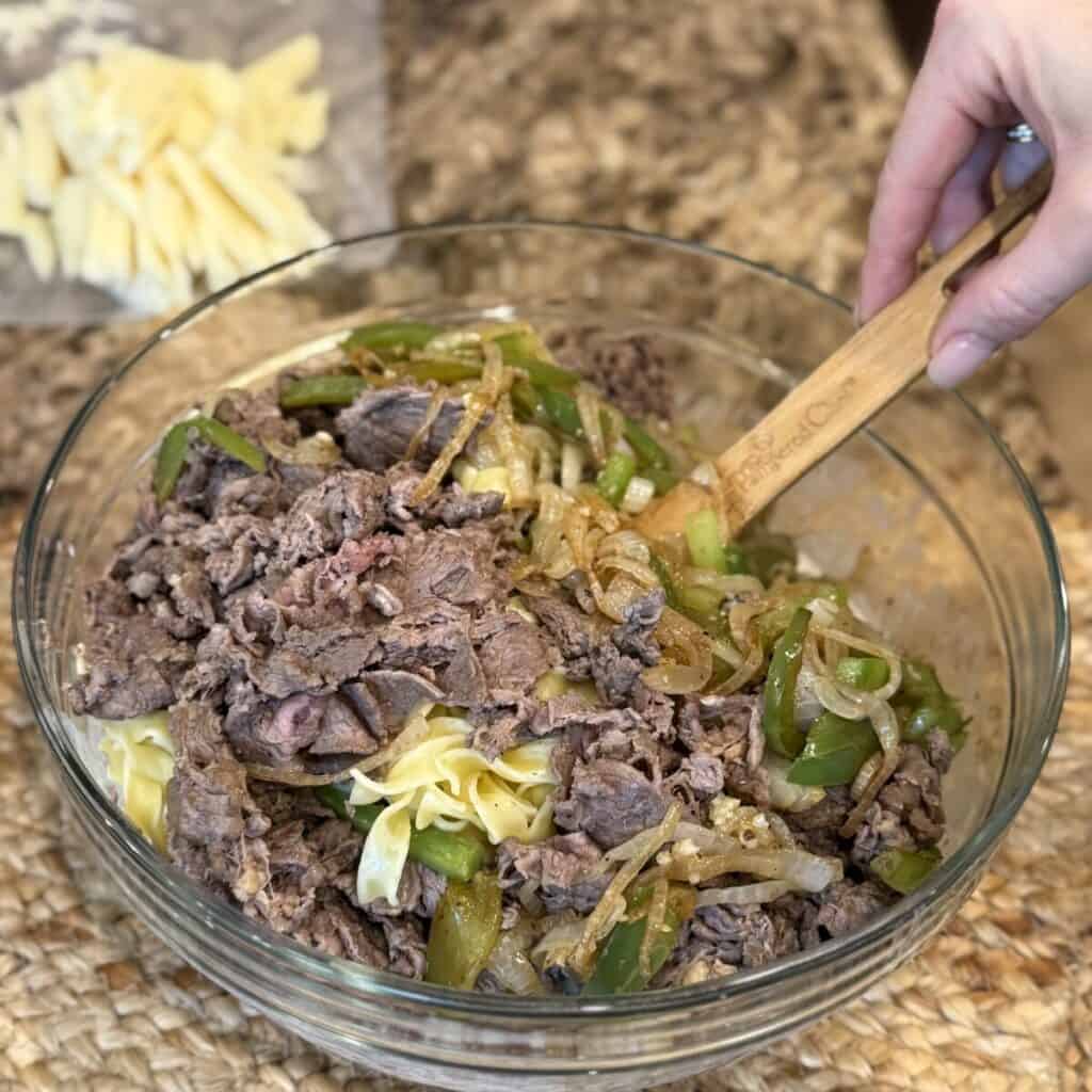 Mixing philly cheesesteak casserole ingredients in bowl.