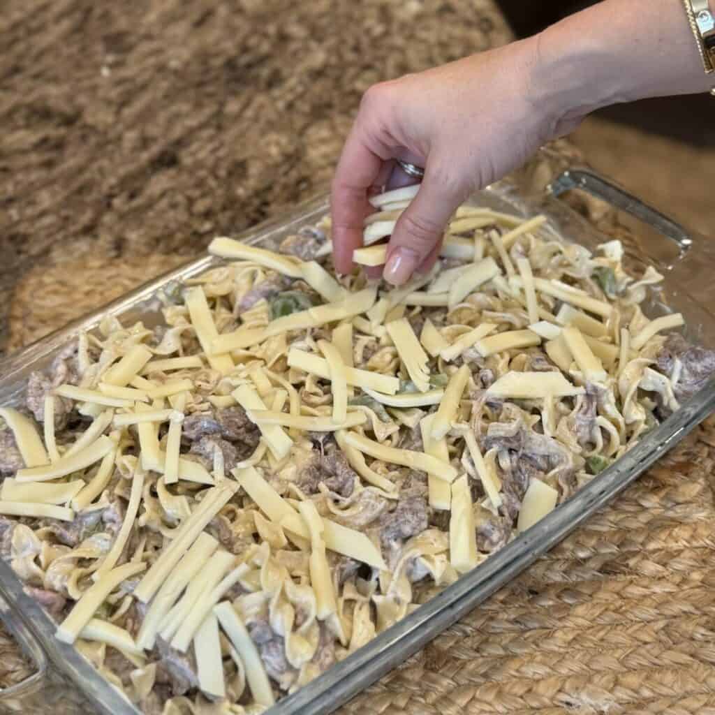 Adding provolone to the top of a philly cheesesteak casserole.