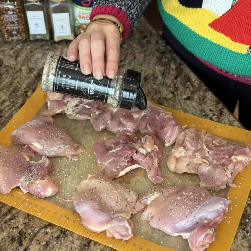 Seasoning chicken with seasoning salt on a cutting board.