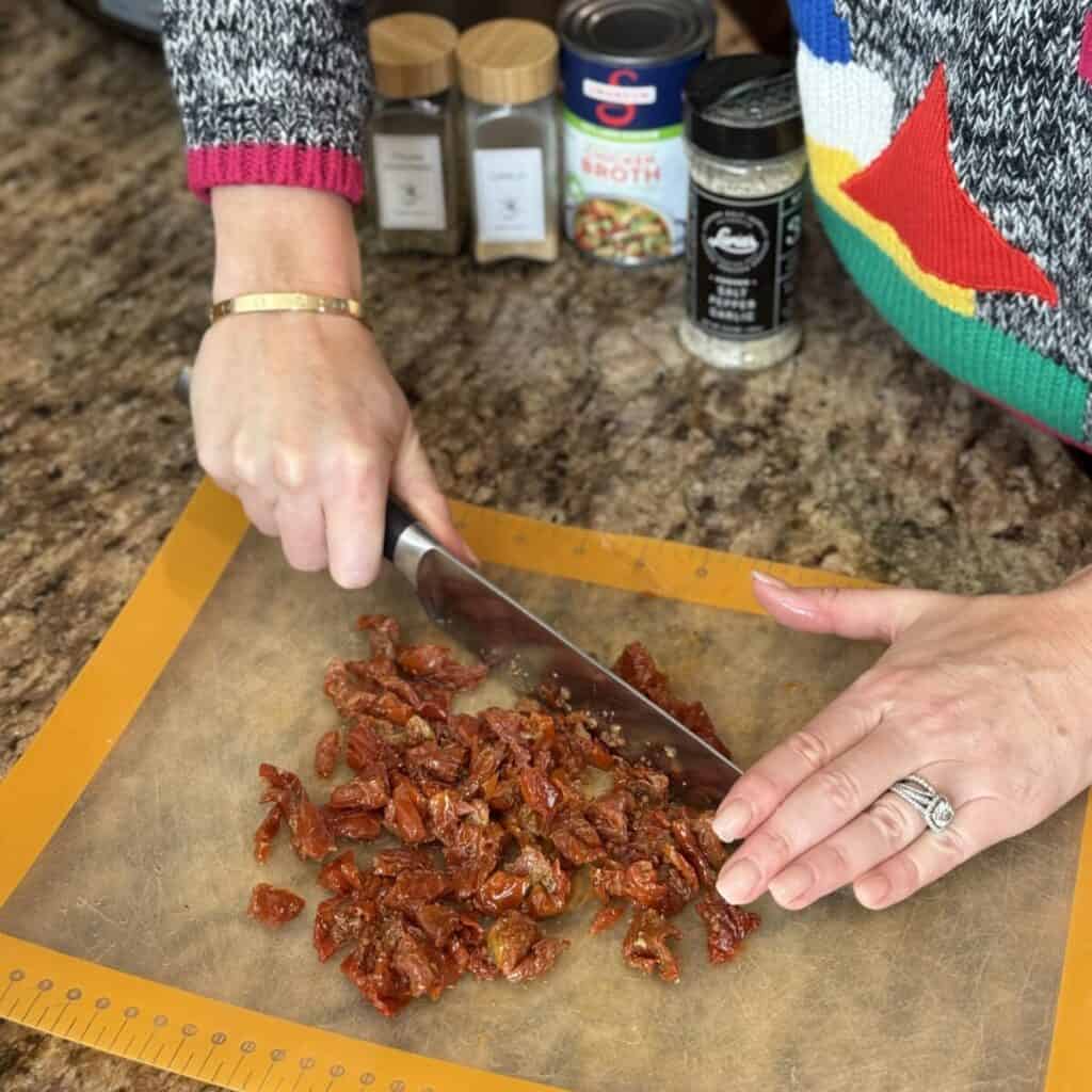 Chopping sundried tomatoes on a cutting board.