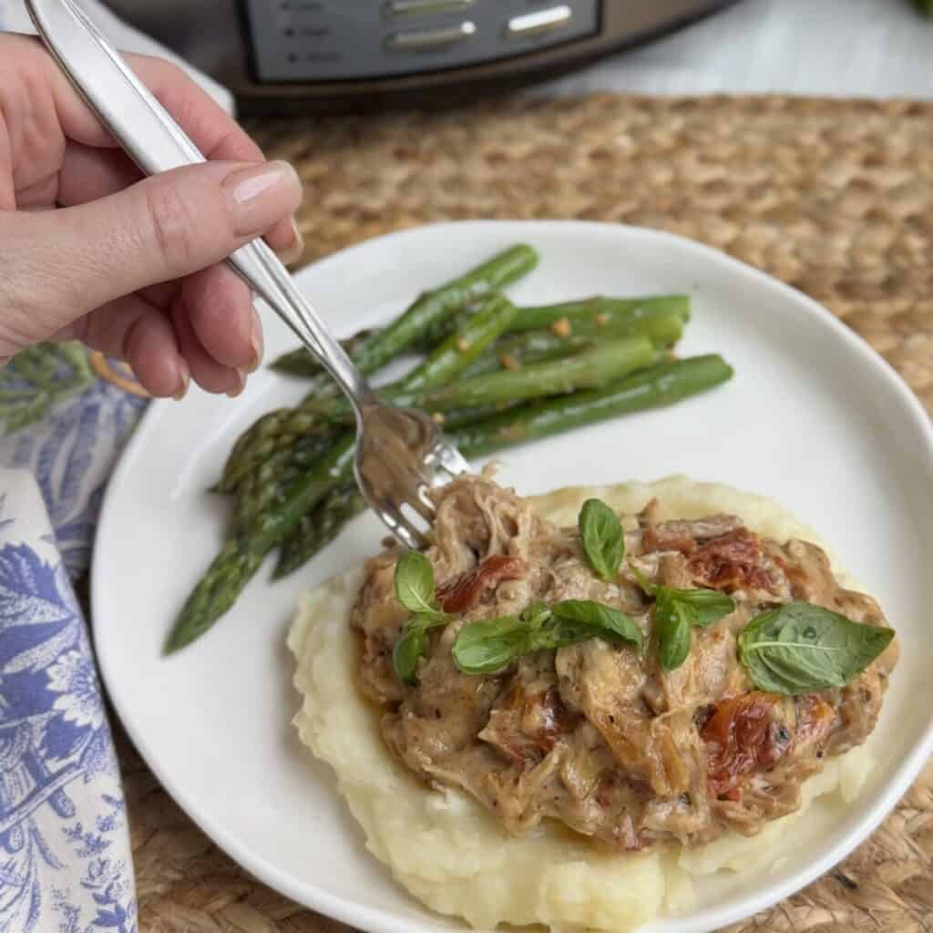 A serving of crock pot marry me chicken on a plate with potatoes and green beans.