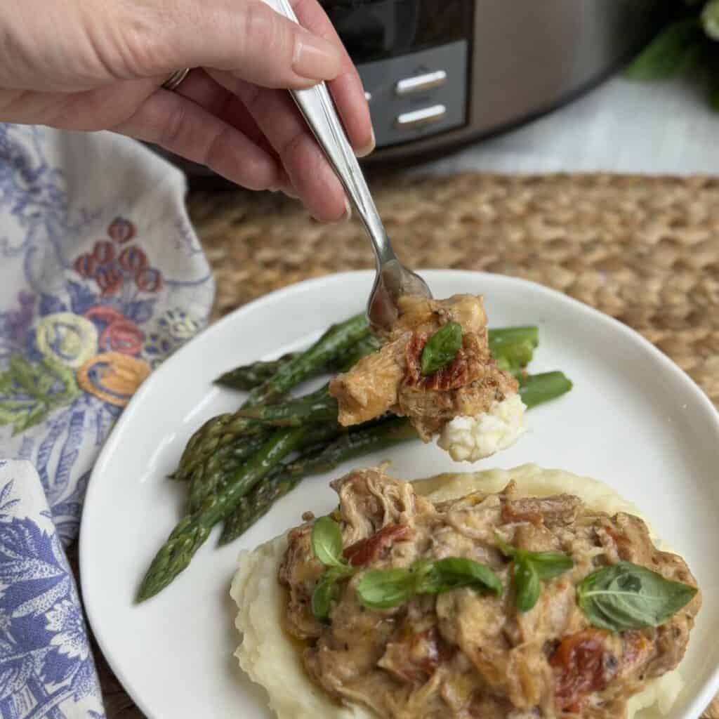 A serving of crock pot marry me chicken on a plate with potatoes and green beans.