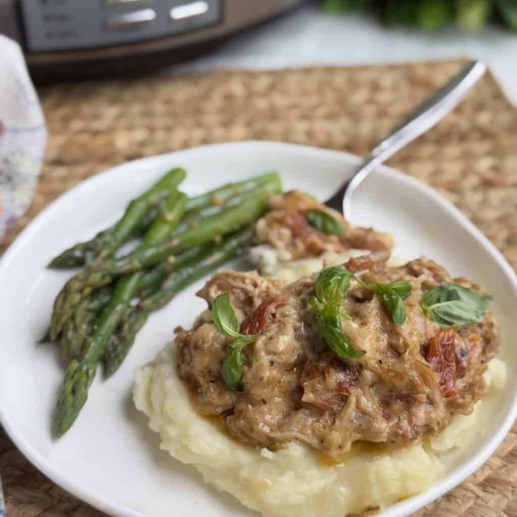 A serving of crock pot marry me chicken on a plate with potatoes and green beans.