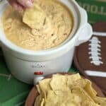 A crockpot of slow cooker taco dip with a chip dipping into it.