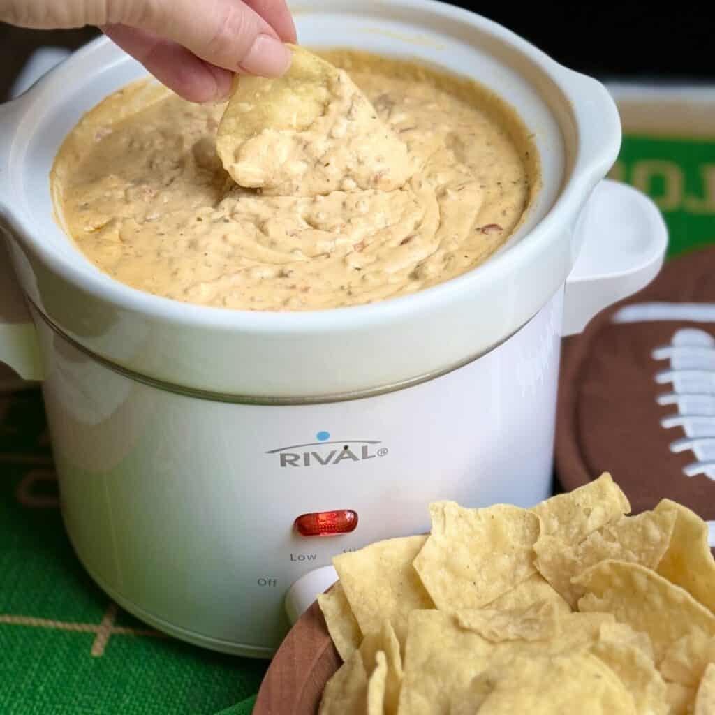 A crockpot of slow cooker taco dip with a chip dipping into it.