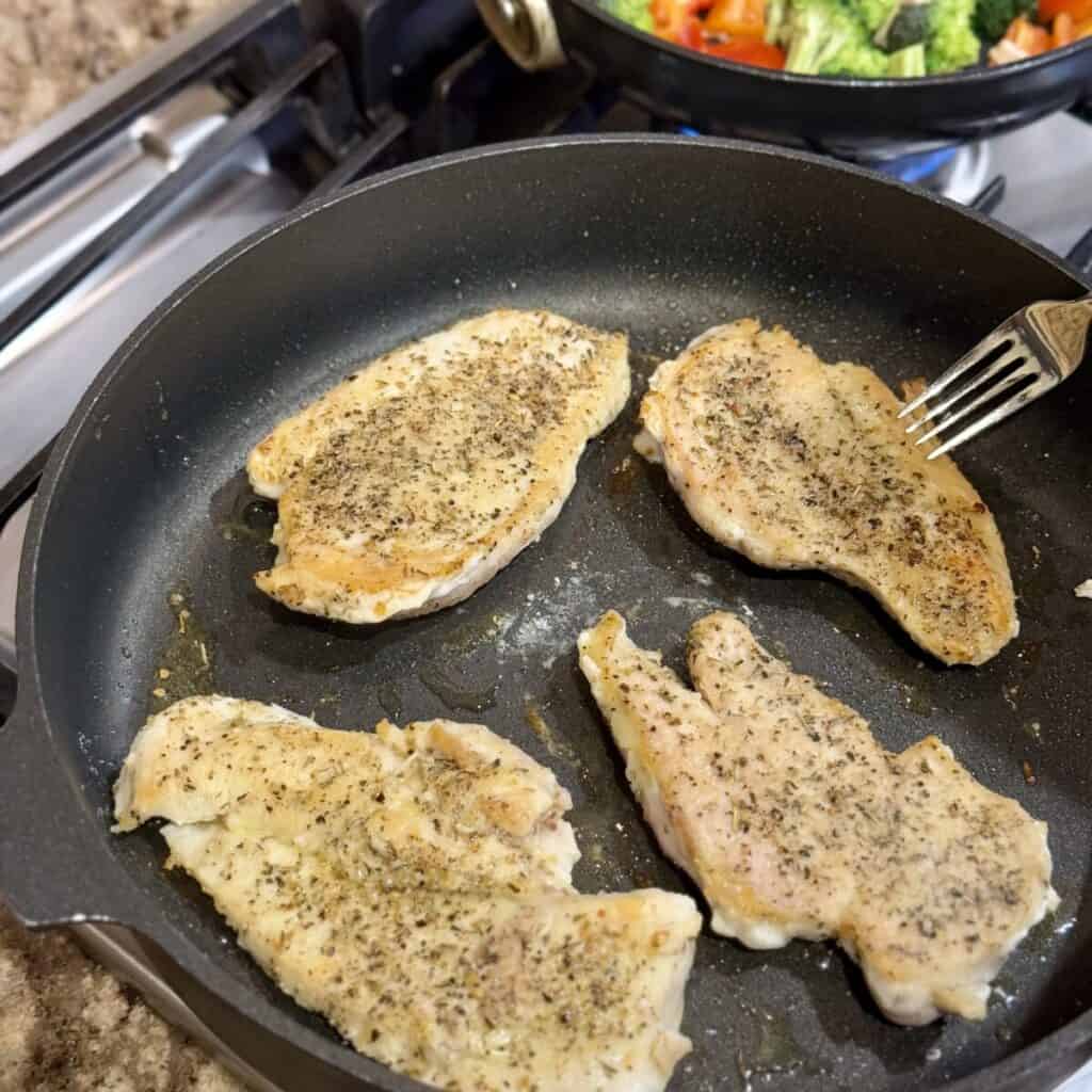 Searing chicken breasts in a skillet.