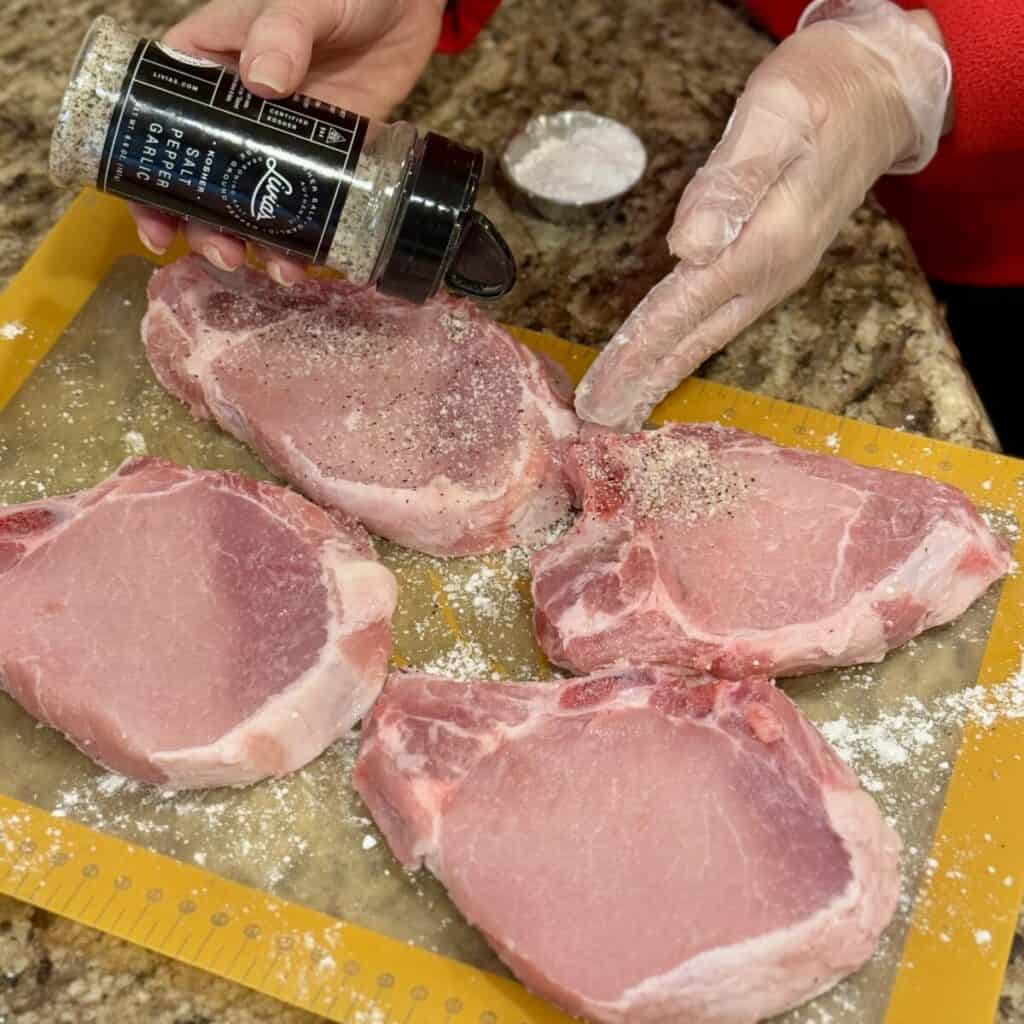 Seasoning pork chops on a cutting board.