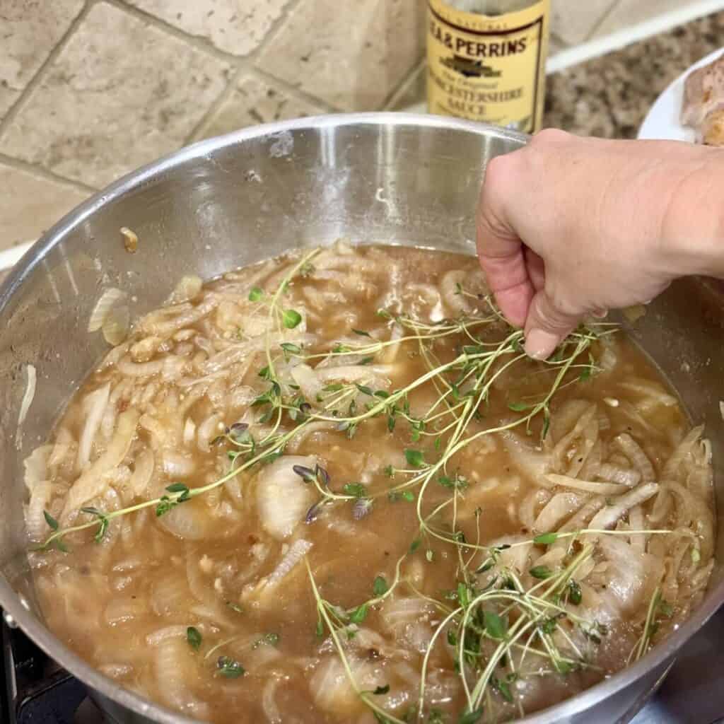 Adding thyme to a skillet of beef broth and onions.