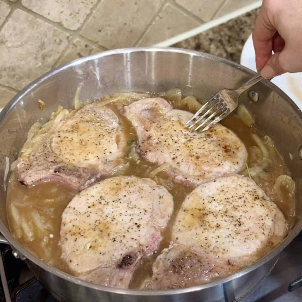 Adding pork chops to broth and onions in a pan.