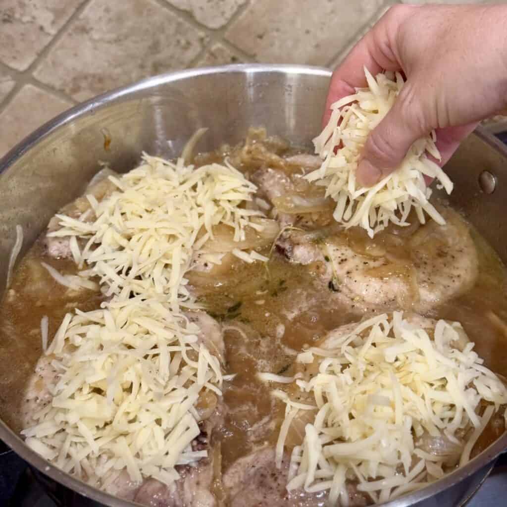 Topping pork chops with shredded cheese in a skillet.