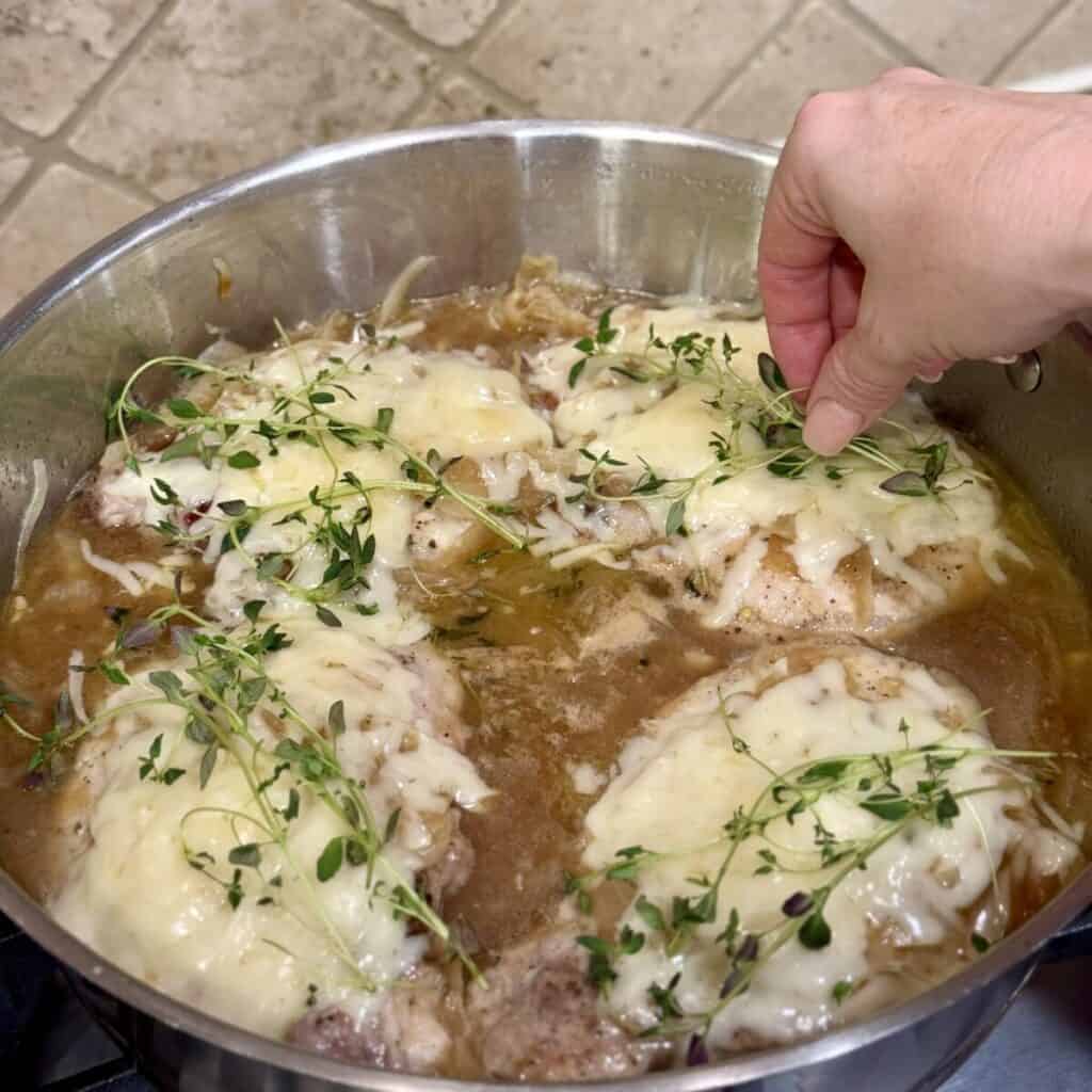 Adding fresh thyme to the top of French onion pork Chops in a pan.