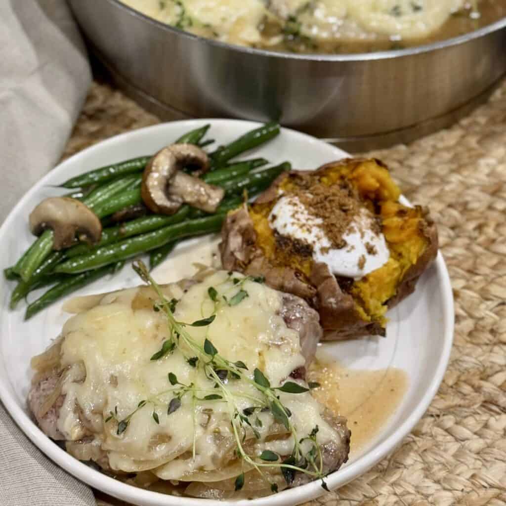 French onion pork chop on a plate with a sweet potato and green beans.