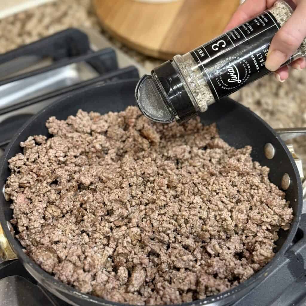 Seasoning ground beef in a skillet.