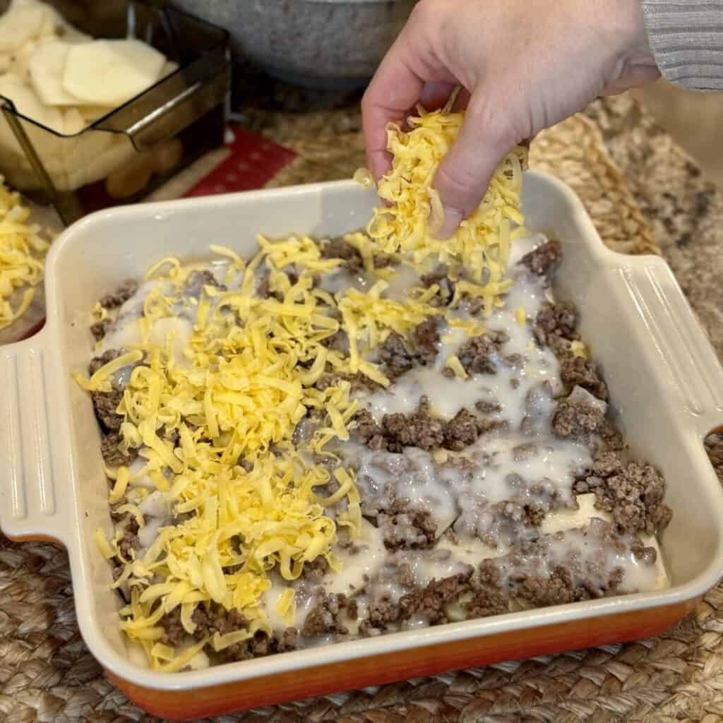 Adding potatoes, beef and cheese to a casserole dish.