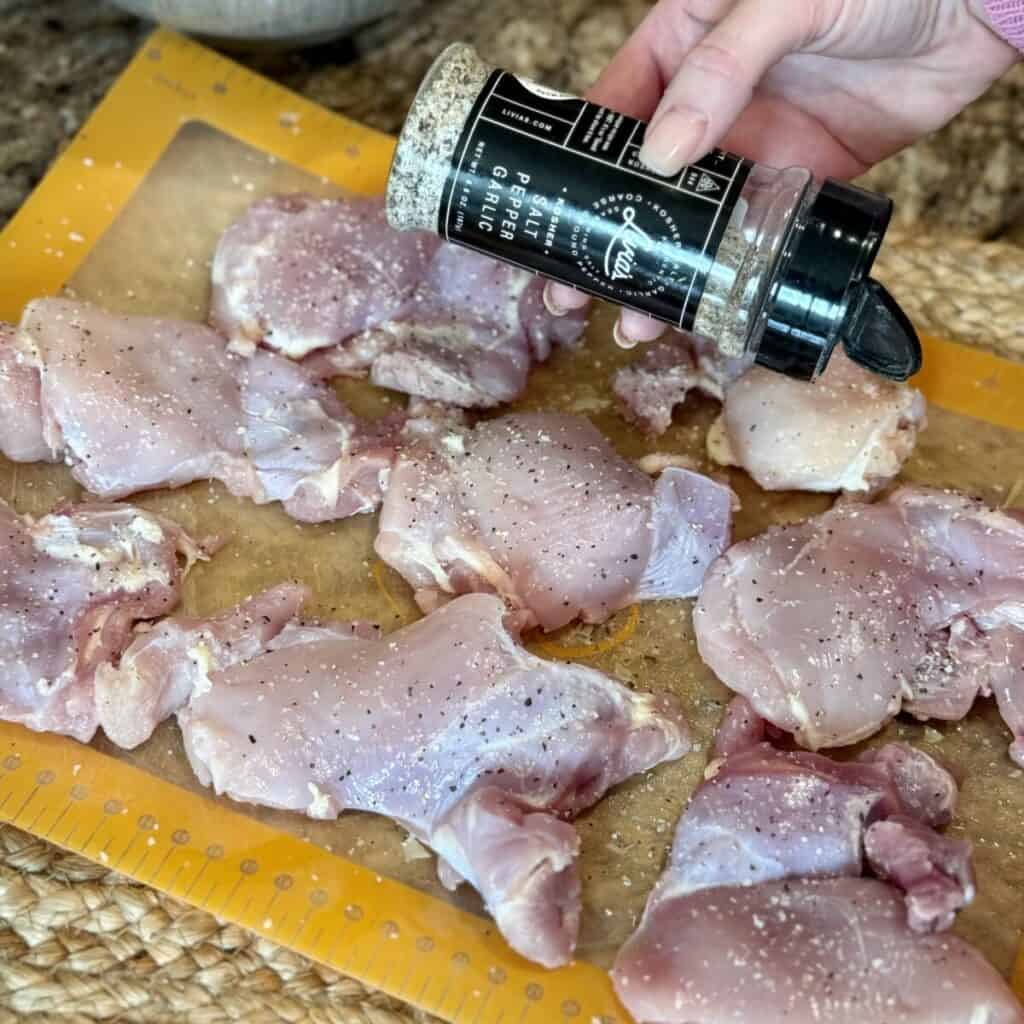 Seasoning chicken thighs on a cutting board.