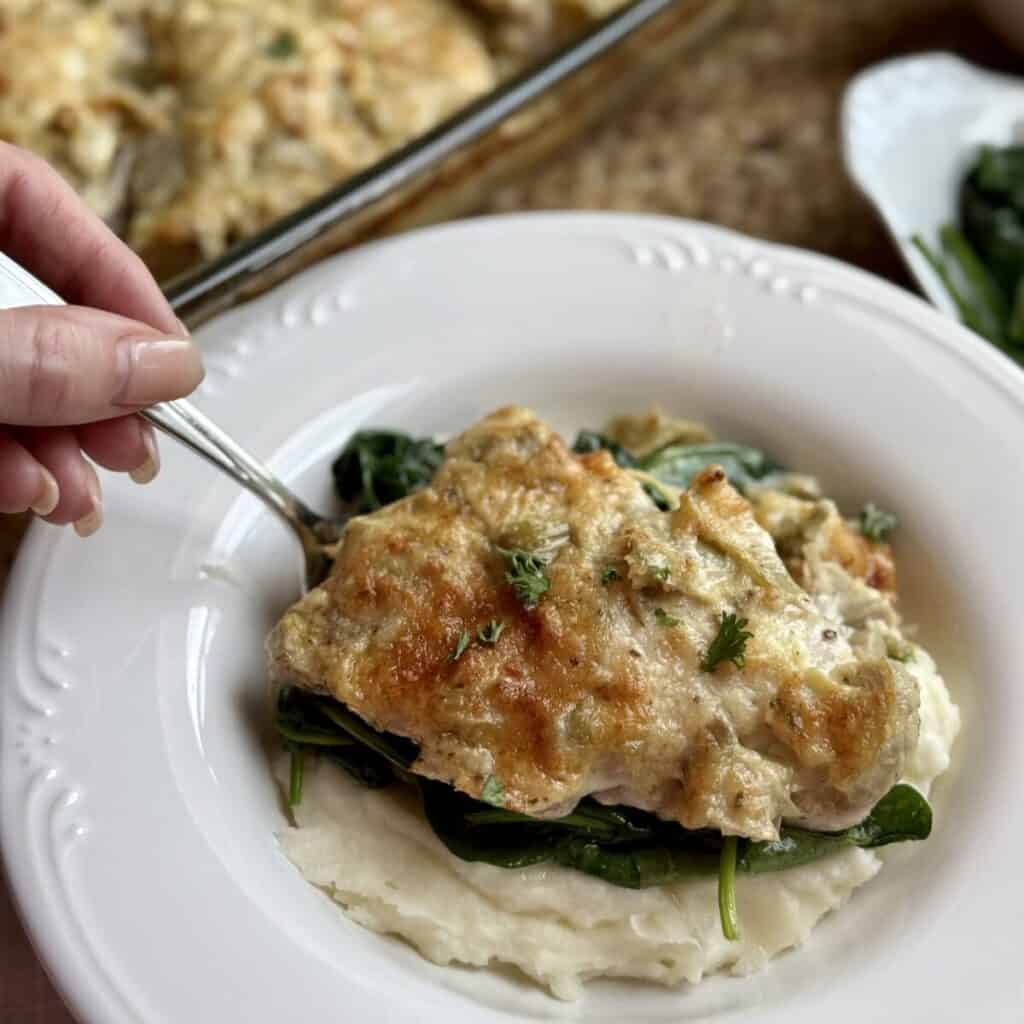 A plate of artichoke chicken, mashed potatoes, and spinach.