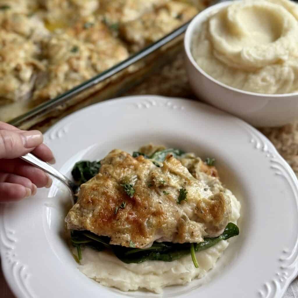 A plate of artichoke chicken, mashed potatoes, and spinach.