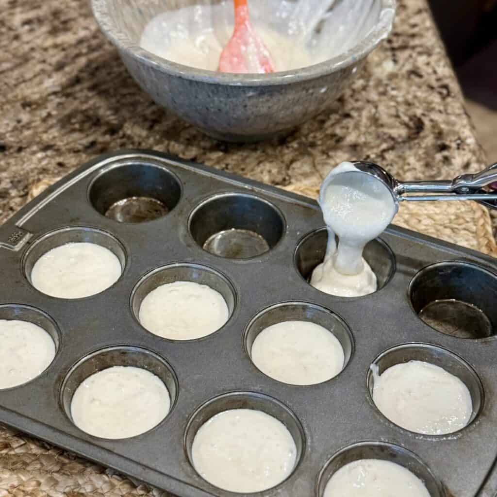 Scooping quick yeast roll batter in a muffin pan.