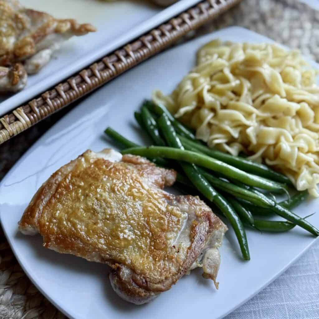 A plate of chicken, noodles and green beans.