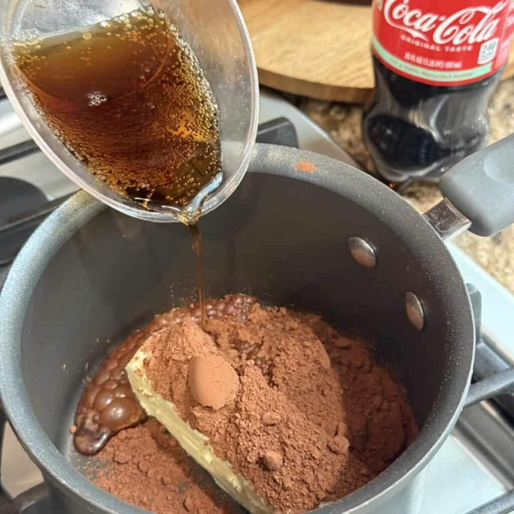 Adding coke to cocoa powder and butter in a saucepan.