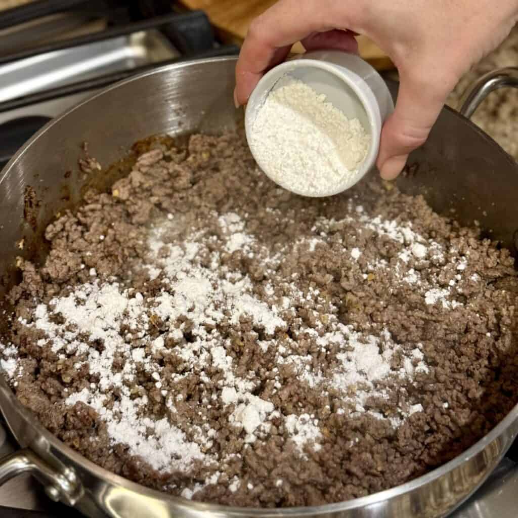 Adding flour to ground beef in a skillet.