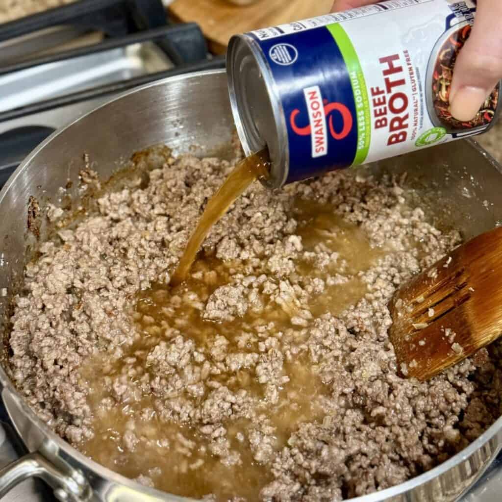 Adding broth to beef in a skillet.