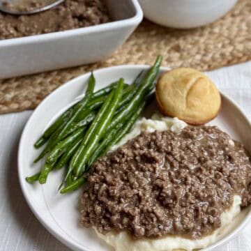 A plate of mashed potatoes, ground beef with gray, and green beans.