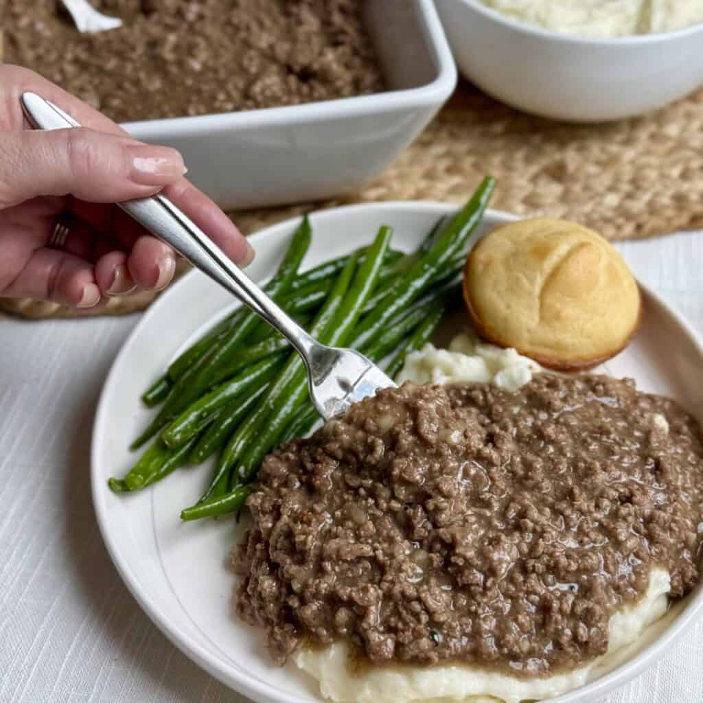 A plate of mashed potatoes, ground beef with gray, and green beans.