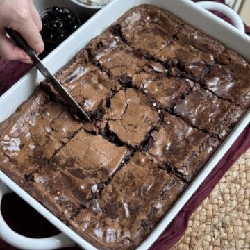 A chocolate ooey gooey butter cake in a baking dish being sliced.